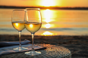 Glasses of delicious wine on riverside at sunset