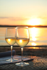 Glasses of delicious wine on riverside at sunset