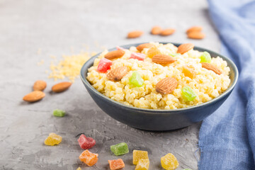 Millet porridge with candied fruits and almonds in blue ceramic bowl on a gray concrete background. Side view, selective focus.
