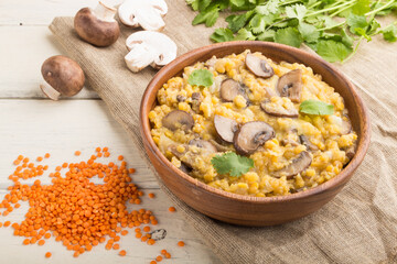 Lentils porridge with champignons. and coriander in a wooden bowl on a white wooden background. Side view.