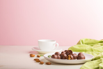 Chocolate caramel candies with almonds and a cup of coffee on a white and pink background. side view, copy space