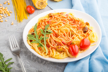 Corn noodles with tomato sauce and arugula on a gray concrete background. Side view.