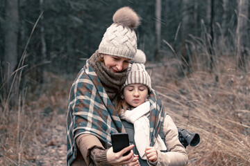 Fototapeta premium Mom and daughter are taking a selfie. Autumn forest background. Winter clothes fashion