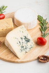 Blue cheese and various types of cheese with rosemary and tomatoes on wooden board on a white background . Side view, selective focus.