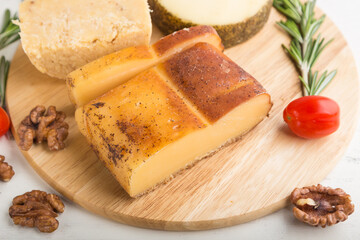 Smoked cheese and various types of cheese with rosemary and tomatoes on wooden board on a white background . Side view, selective focus.