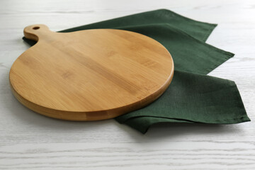 Empty wooden board and green napkin on white table, closeup