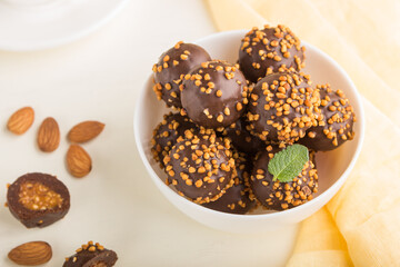 Chocolate caramel ball candies with almonds and a cup of coffee on a white wooden background. Side view, selective focus.