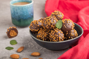 Chocolate caramel ball candies with almonds and a cup of coffee on a gray concrete background and red textile. Side view, selective focus.