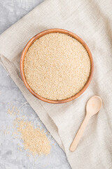 Wooden bowl with raw white quinoa seeds and wooden spoon on a gray concrete  background. Top view, close up.