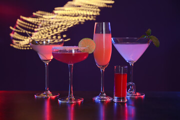 Many different alcoholic drinks on table against dark background with blurred lights