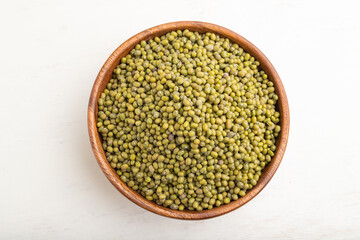 Wooden bowl with raw green mung bean on a white wooden background. Top view, close up.