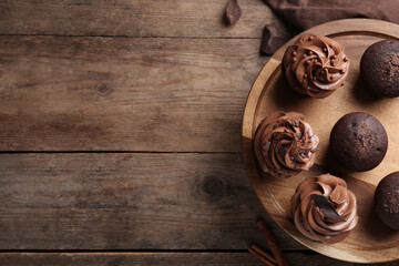 Delicious chocolate muffins and cupcakes decorated with cream on wooden table, top view. Space for text