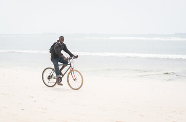 Fototapeta na wymiar African young man riding bike on tropical beach
