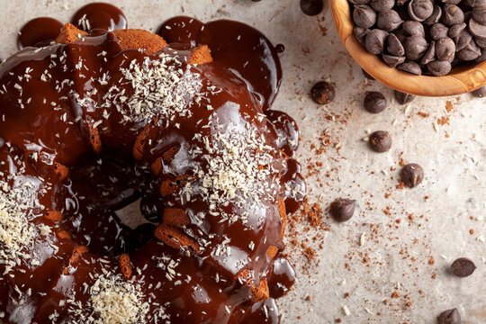 Flat lay image of a Chocolate cake with melted  pudding icing and chocolate chips in a bowl in the background. The decoration of this delicious cake was finished with sprinkles of shredded coconuts.