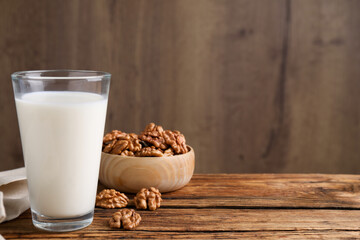 Glass of walnut milk on wooden table, space for text