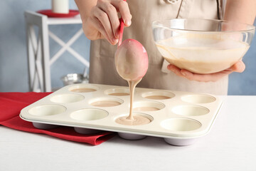 Woman pouring batter into cupcake tray at white table in kitchen, closeup