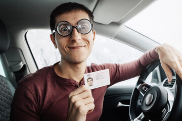 Funny nerd and geek in huge ridiculous glasses shows his driver's license. Concept of vision...