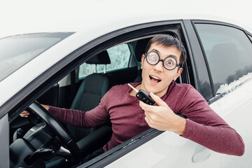 Funny driver in eye glasses holding the car key and smiling to the camera. Concept of a newbie driver and insurance