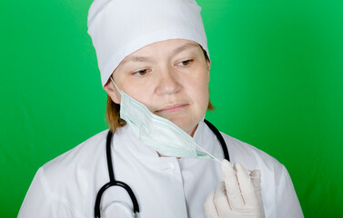 Female doctor with phonendoscope on her neck tiredly removes a protective mask from face