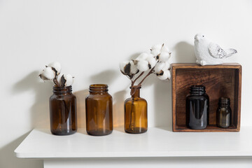 A row of brown small pharmacy bottles instead of vases with branches of blossoming cotton and wooden boxes on a white surface of the fireplace