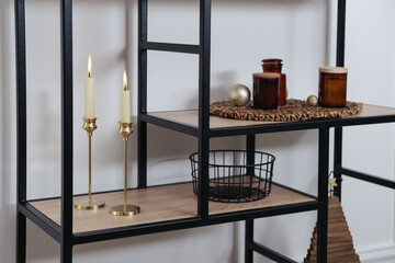 Stylish shelving unit with burning candles and decor near white wall indoors. Interior design