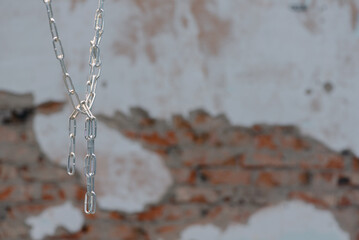 An old metal chain hanging from the roof on the old brick wall background.