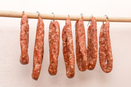 Drying Sausages From Raw Minced Meat In Limbo On A Wooden Stick On A White Wall Background At Home