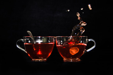 Fototapeta na wymiar A piece of rock sugar is splashing into one of two glass cups of tea in front of a black background