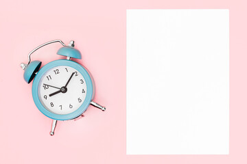 Alarm clock and blank sheet on a pink background.