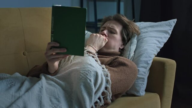 Seek handsome guy is reading book lying at the sofa under the blanket 