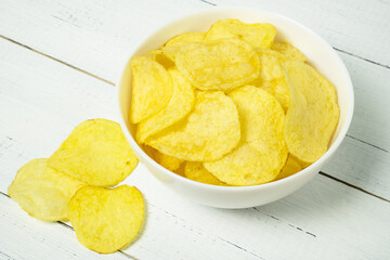 Natural potato chips in ceramic bowl on wooden table.