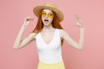 Young caucasian redhead woman 20s ginger long hair wearing straw hat glasses summer clothes show blah blah gesture ja jaja hands looking aside isolated on pastel pink color background studio portrait. © ViDi Studio
