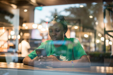 Young authentic black woman sitting with phone in city coffee shop