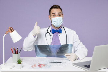 Male happy doctor man wearing medical gown sterile face mask latex gloves hold X-ray of lungs fluorography roentgen show thumb up gesture isolated on violet background Healthcare medicine concept
