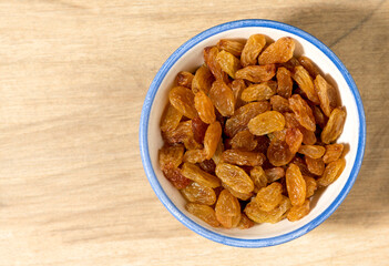 Yellow raisins in a small bowl, top view. Copy space.