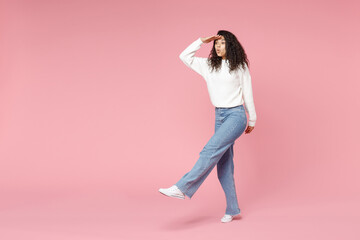 Fototapeta na wymiar Full length young successful overjoyed african american woman 20s curly hair in white knitted sweater jeans hold hand at forehead looking far away distance isolated on pink background studio portrait.