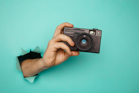 Man's Hand Holding Old Camera From Blue Torn Paper.