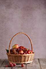 Fototapeta na wymiar Fresh fruit. Grapes and red apples with drops of water in the basket and green leaves on a gray wooden table on grey background. Rustic. Background image, copy space, vertical