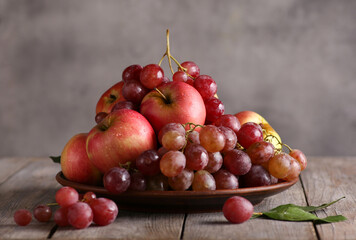 Fresh fruit. A plate of grapes and red apples with drops of water and green leaves on a gray wooden table on grey background. Background image, copy space, horizontal
