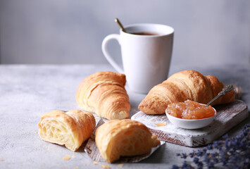 Bakery products and desserts. Classic croissants with jam, a cup of coffee on a light gray background with purple flowers, newspaper. French dough baked on a white board. Background image, copy space