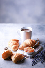 Bakery products and desserts. Classic croissants with jam, a cup of coffee on a light gray background with purple flowers, newspaper. French dough baked on a white board. Background image, copy space