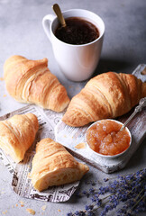 Bakery products and desserts. Classic croissants with jam, a cup of coffee on a light gray background with purple flowers, newspaper. French dough baked on a white board. Background image, copy space