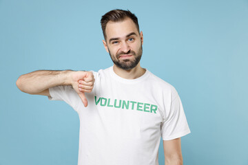 Displeased confused young bearded man in white volunteer t-shirt showing thumb down looking camera...