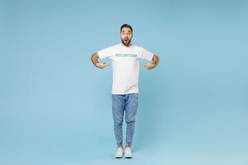 Fototapeta na wymiar Full length of shocked young bearded man 20s in white volunteer t-shirt pointing index fingers on himself isolated on blue background studio. Voluntary free work assistance help charity grace concept.