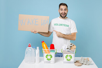Excited man in volunteer t-shirt stand near recycling stations sorting plastic paper trash point nameplate wake up isolated on blue background. Voluntary work assistance help charity grace concept.