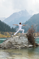 Yoga man in warrior pose on mountain lake rock, ourdoor activities concept.