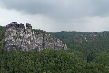 Fototapeta na wymiar Huge black grey colored and fissured sandstone rock formations surrounded by green forest; Saxon Switzerland, Germany, Europe
