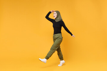 Fototapeta na wymiar Full length of excited young arabian muslim woman in hijab black green clothes looking far away distance isolated on bright yellow color background studio portrait. People religious lifestyle concept.