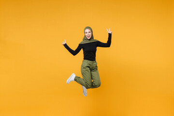 Fototapeta na wymiar Full length excited young arabian muslim woman wearing hijab black green clothes jumping showing victory sign isolated on yellow color background studio portrait. People religious lifestyle concept.