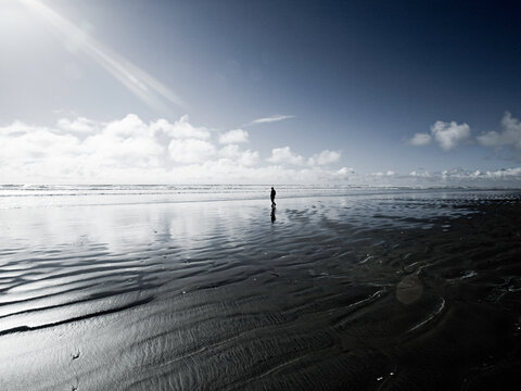 A cloudy day at the beach in Gearhart, Oregon. A lone figure walks out into the shallow waters as the tides recede.